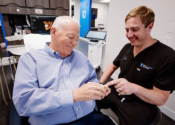 Dr. Bill Keith showing elderly patient tooth model at Keith & Associates Dental Implant Center in Mission, KS.
